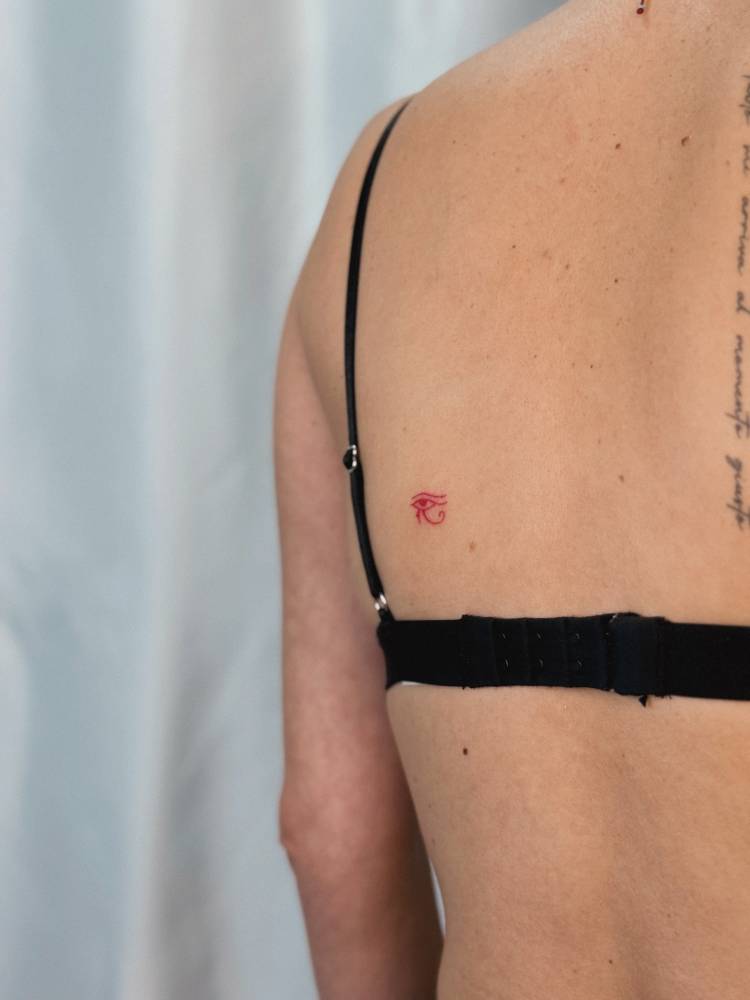 Minimalistic style Eye of Horus tattoo in red ink located on the shoulder blade.