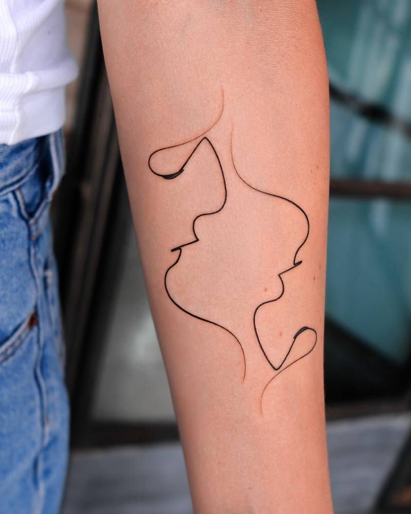 Abstract faces tattooed on the inner forearm, original artwork by Quibe.