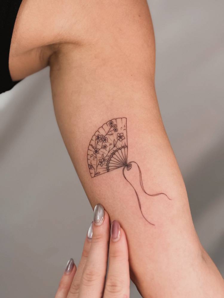 Hand fan tattoo in fine line style located on the inner arm.