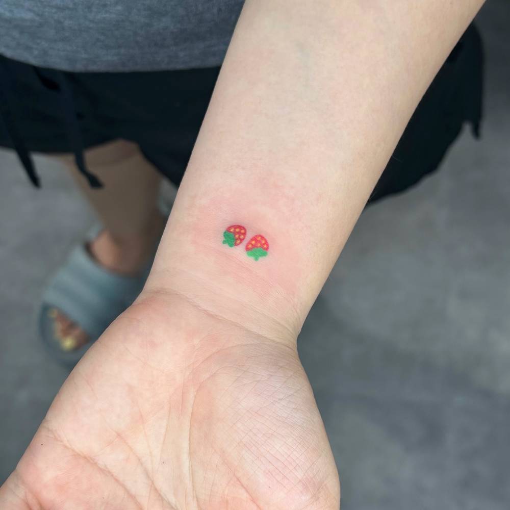 Tiny minimalistic strawberries tattoo hand poked on the wrist.