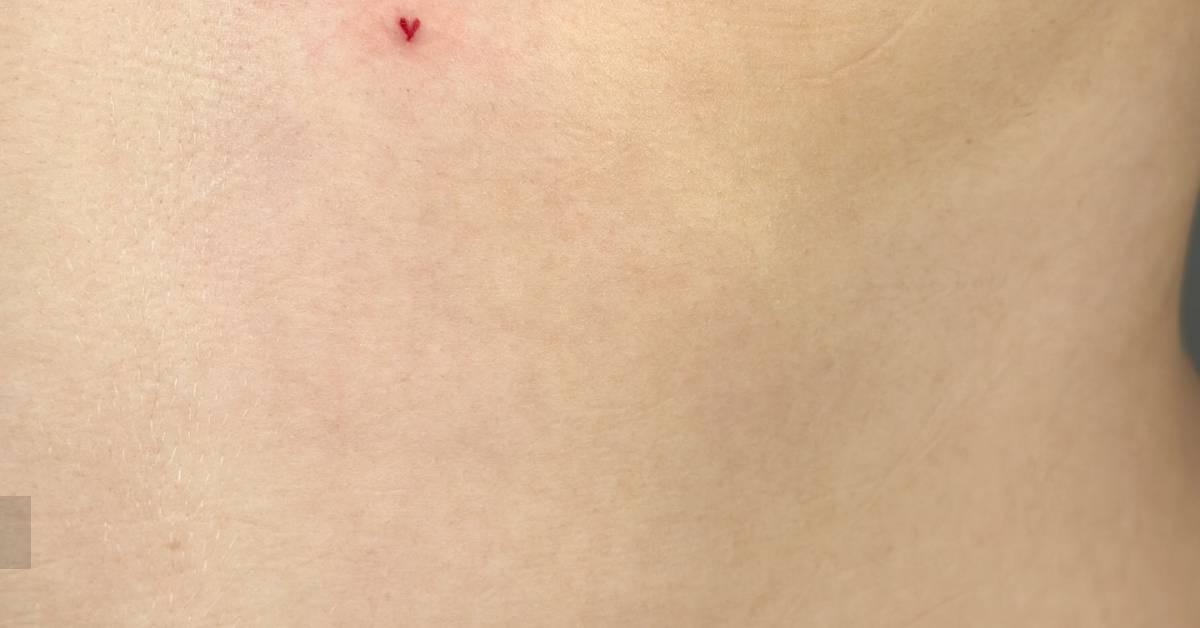 Tiny red heart tattoo in minimalistic style placed on
