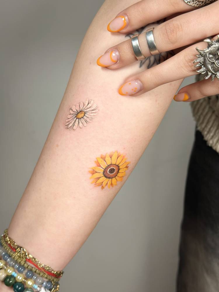 Daisy and sunflower tattoo in watercolor style located on the inner forearm.