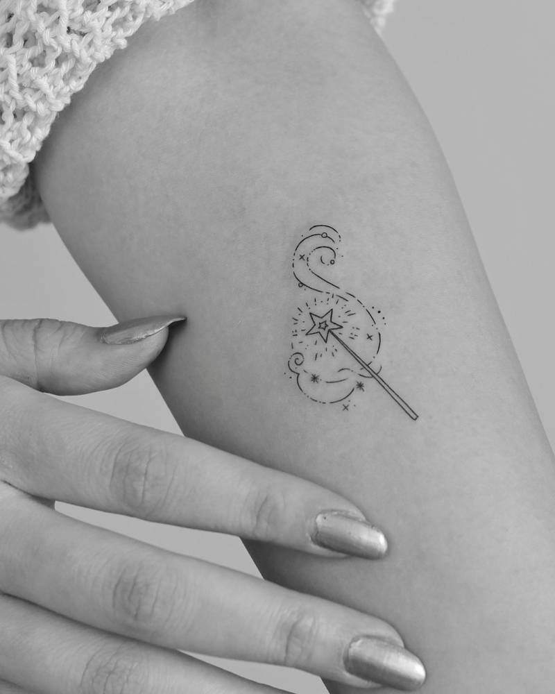 Magic wand tattoo in fine line style located on the inner forearm.