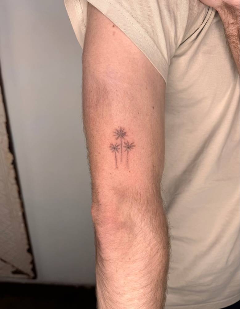 Palm trees tattoo located on the upper arm, done in fine line style.