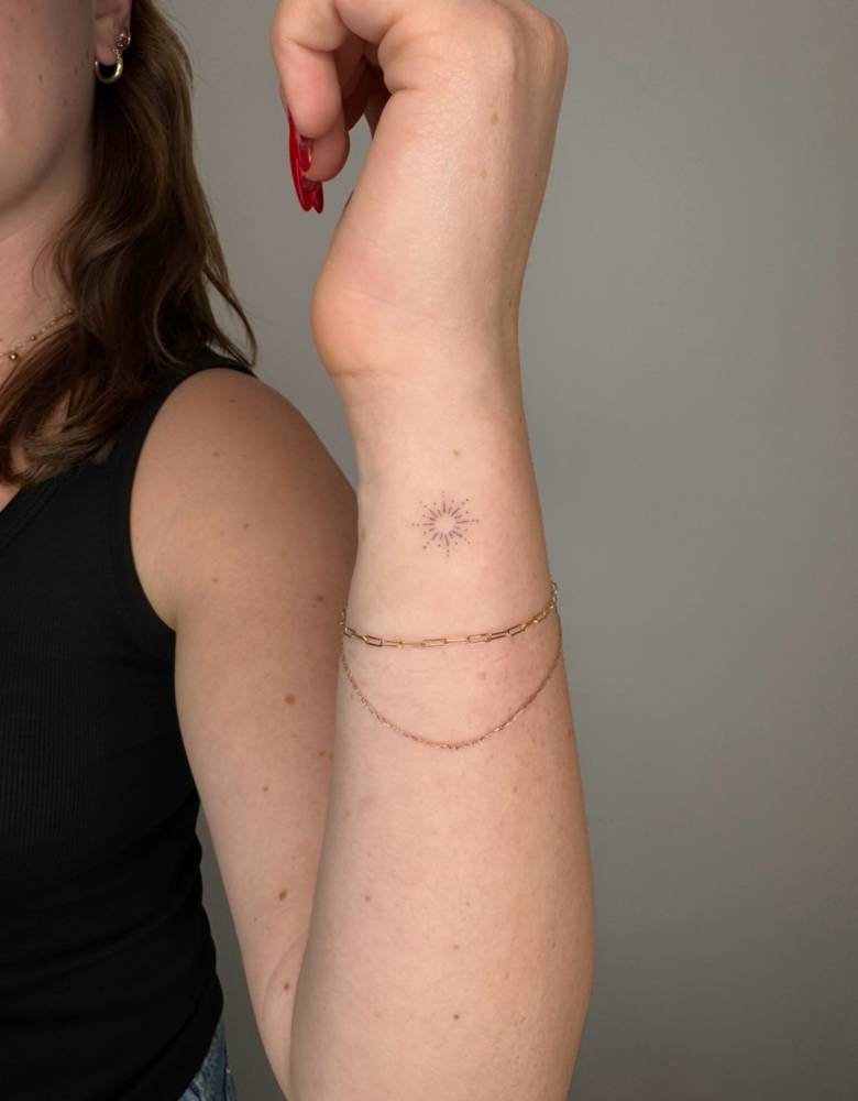 Sun tattoo in fine line style placed on the wrist.