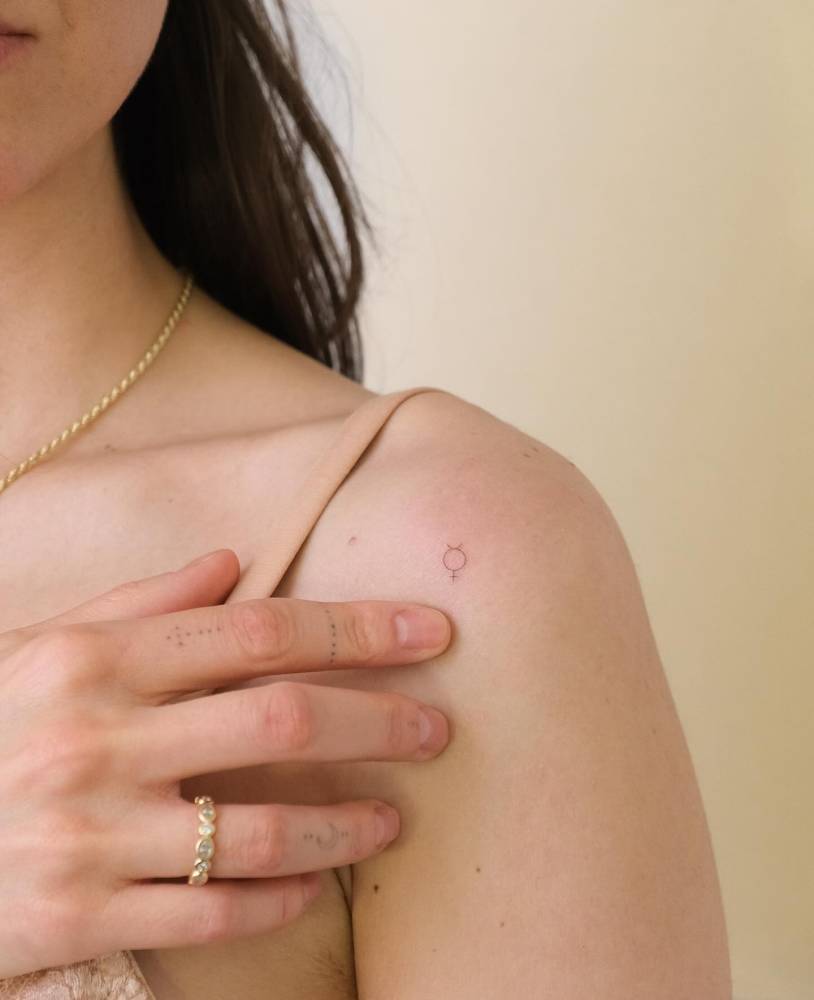Minimalistic style tiny Mercury planet symbol tattooed on the shoulder.