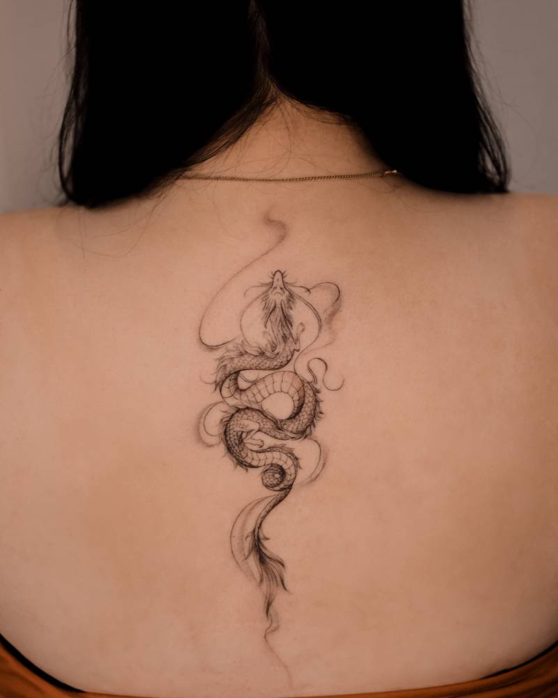 Dragon tattoo in illustrative style located on the upper back.