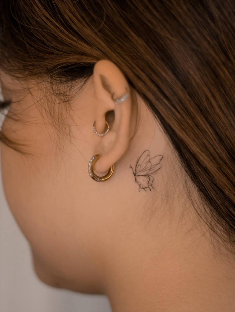 Tiny butterfly tattoo in fine line style located behind the ear.