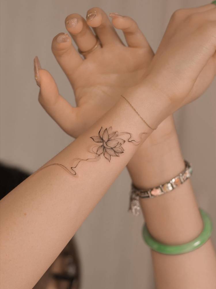 Lotus flower tattoo in illustrative style located on the wrist.