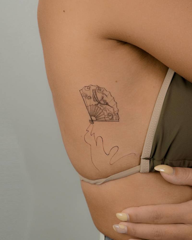 Hand fan tattoo in illustrative style done on the side boob.