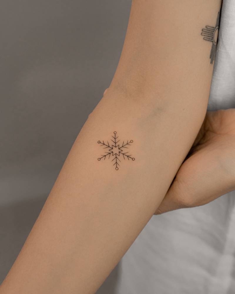 Fine line style snowflake tattoo located on the inner forearm.