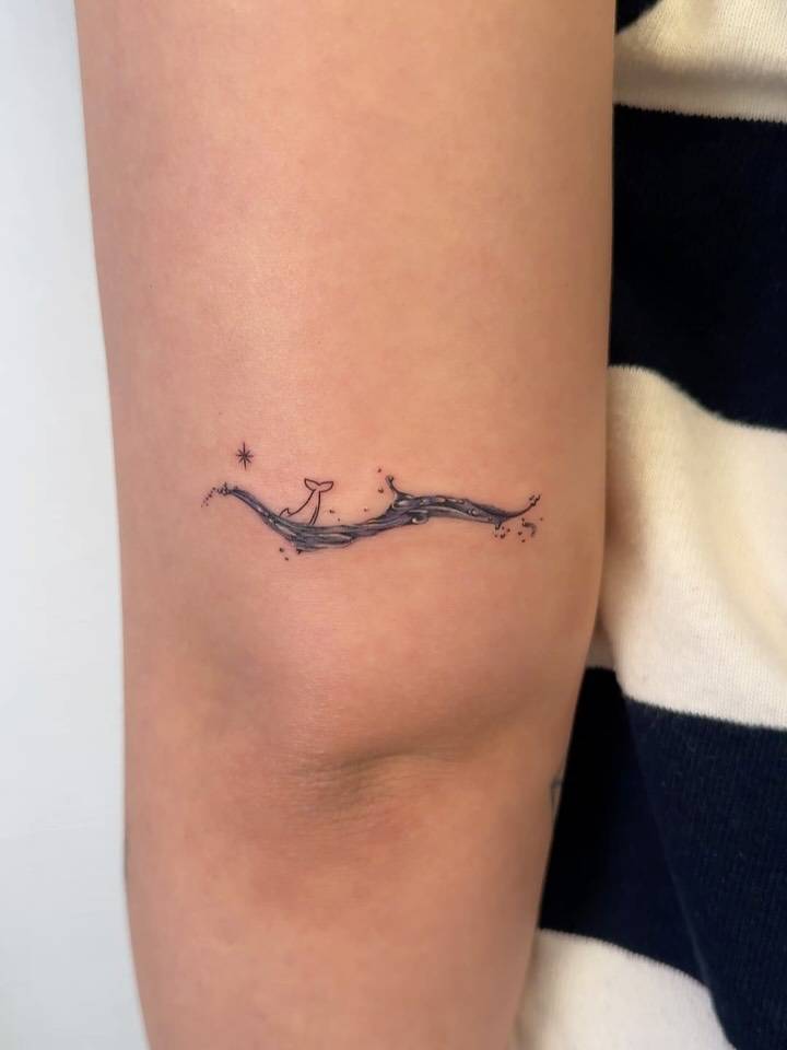 Dolphin and waves tattoo in illustrative style located on the tricep.