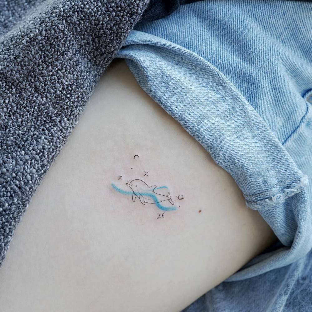 Cute space dolphin tattoo located on the thigh.