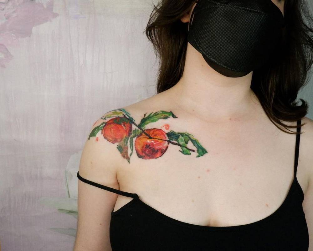 Peaches tattooed on the shoulder and collarbone, watercolor style.