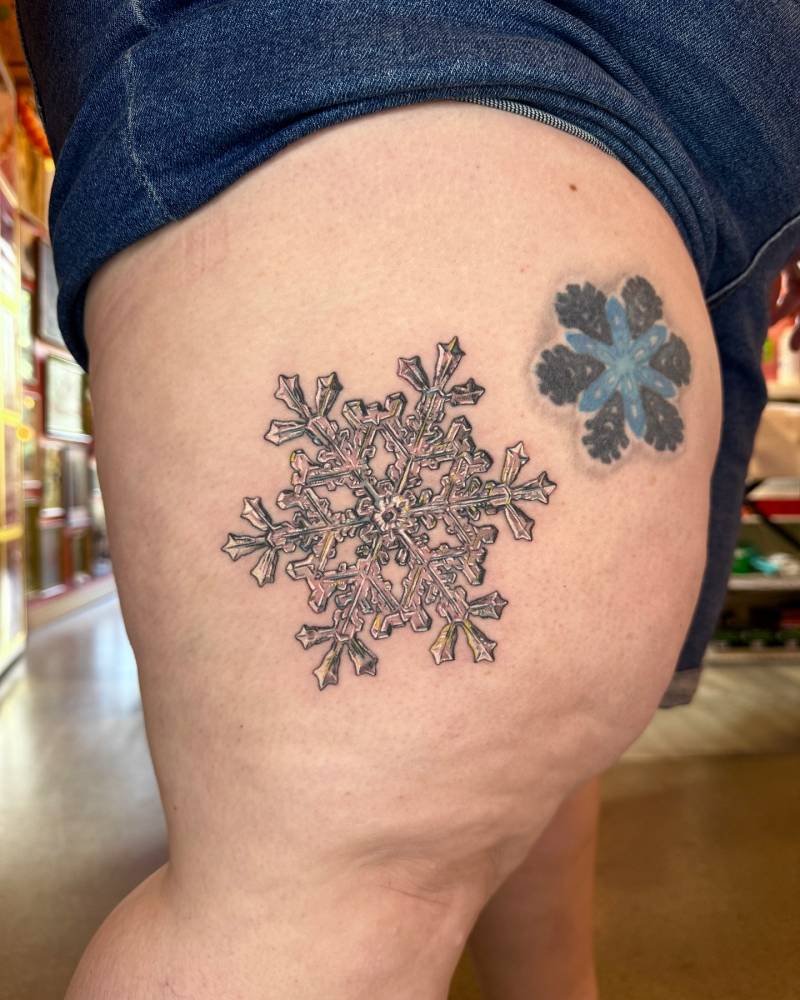 Snowflake tattoo in illustrative style located on the thigh.