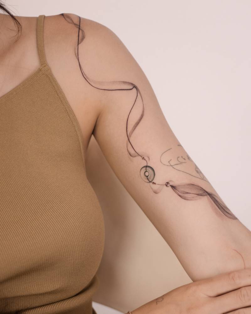 Norigae tattoo located on the bicep and shoulder, done in illustrative style.