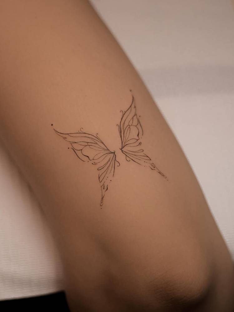 Butterfly tattoo in fine line style located on the tricep.