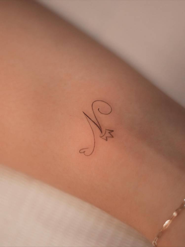 Tiny letter "N" and crown tattoo located on the wrist.
