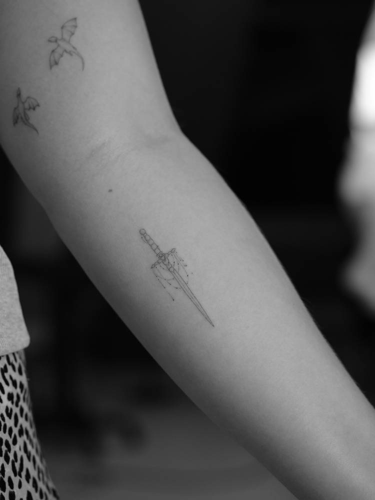 Fine line style sword tattoo located on the inner forearm.