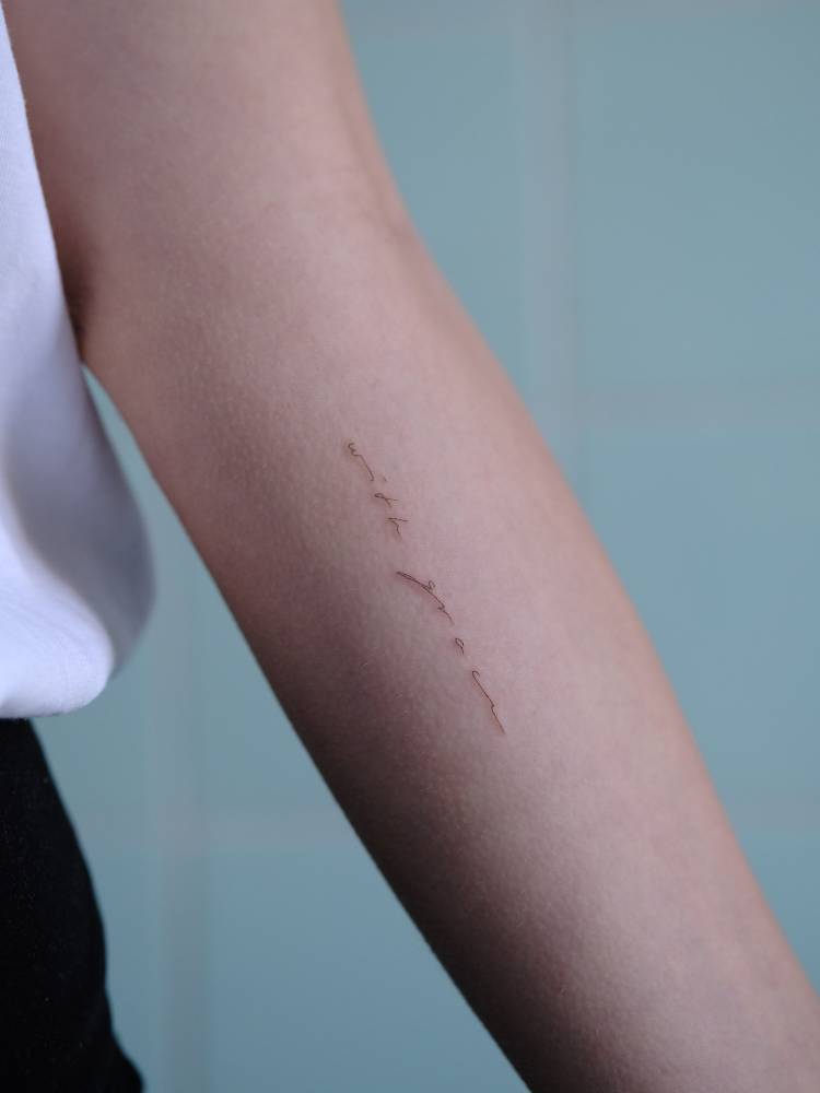 "With grace" lettering tattoo in handwritten font located on the inner forearm.