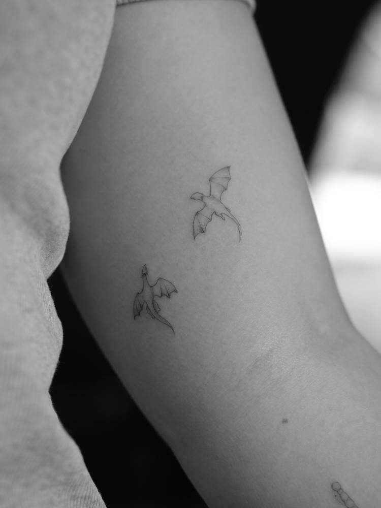 Tiny little dragons tattooed on the inner arm, minimalistic style.