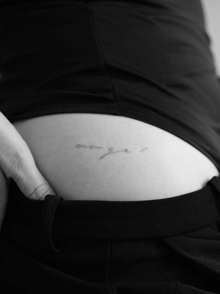 Handwritten font word "angel" tattooed on the hip.