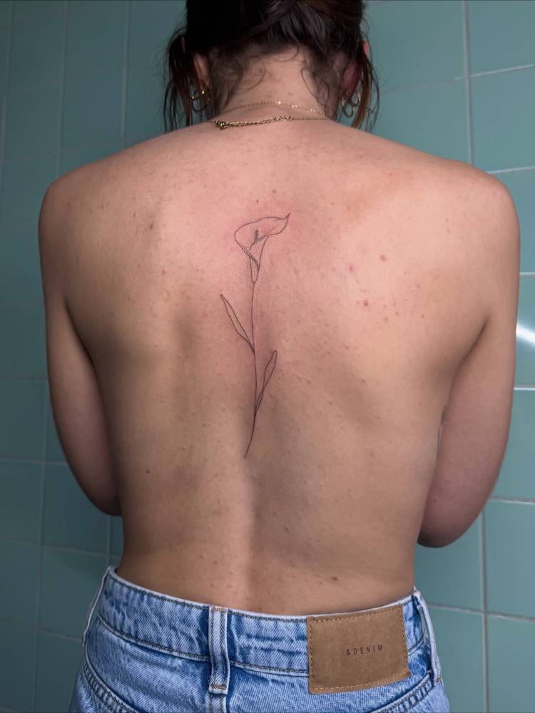 Calla lily tattoo in fine line style located on the spine.