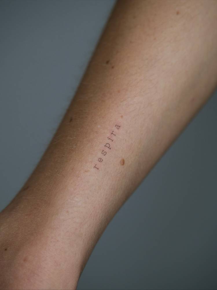 Typewriter font word "respira" tattooed on the wrist.
