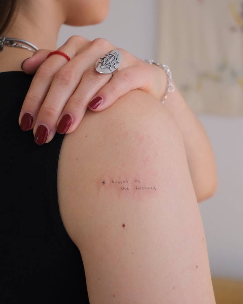 Handwritten font "kisses on the forehead" tattoo located on the upper arm.