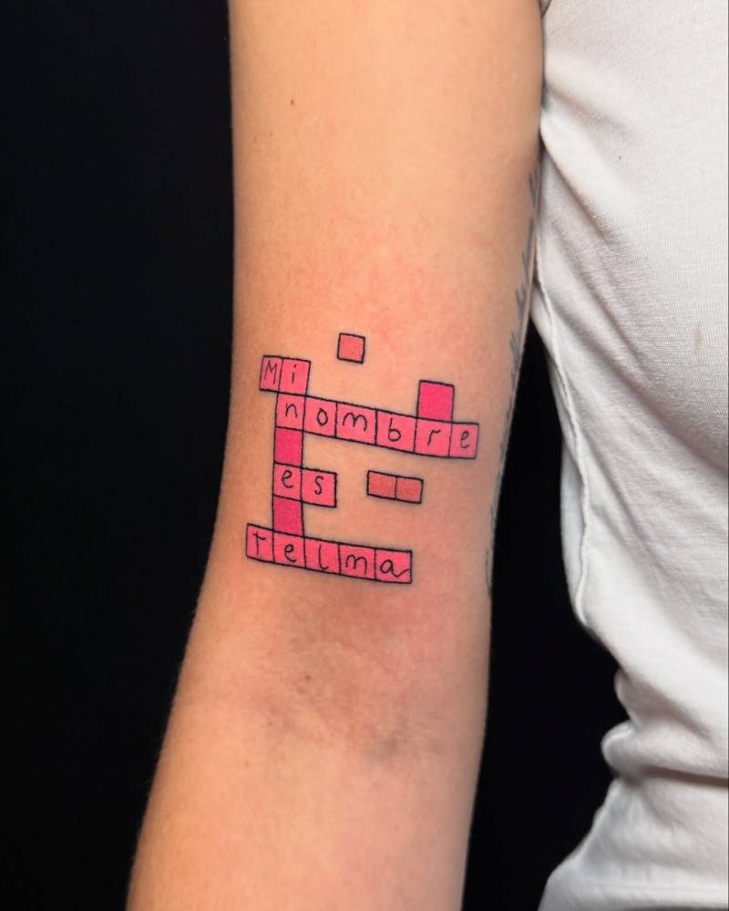 Hand poked crossword tattoo in cartoon style located on the bicep.