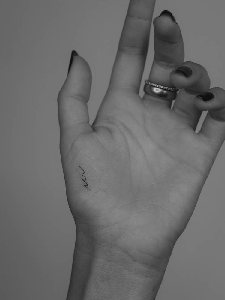 word "ici" tattoo in handwritten font located on the palm.