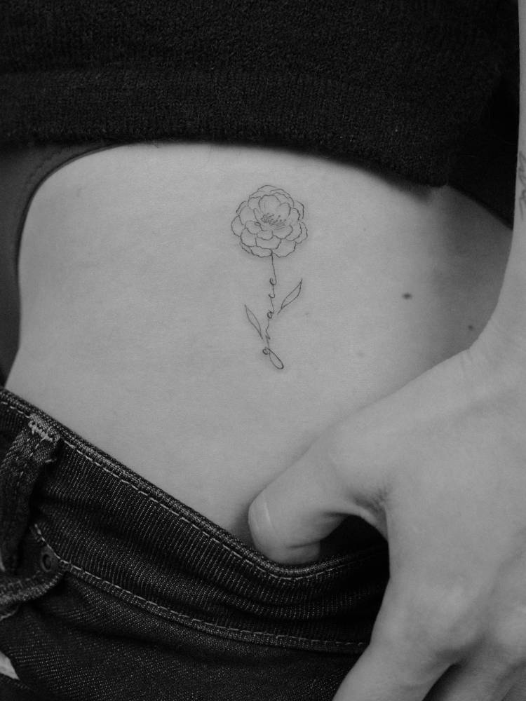 Fine line style peony and "grace" tattoo located on the hip.