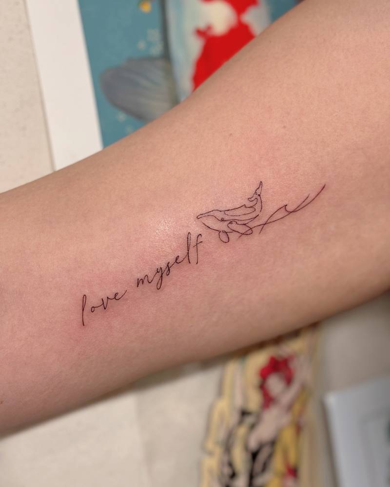 "Love myself" and whale tattoo located on the inner arm.