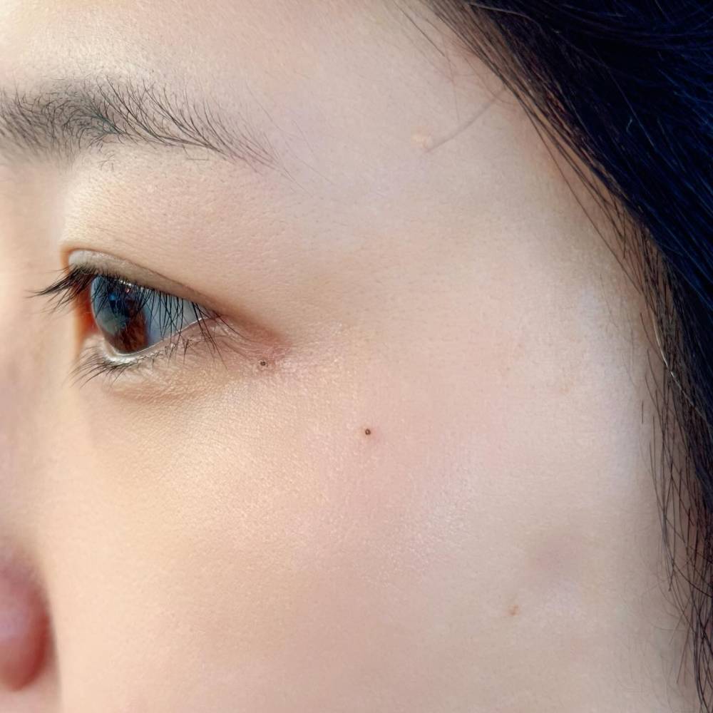 Tiny minimalistic dot tattooed on the face.