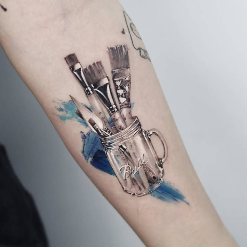 Paintbrushes tattoo located on the inner forearm, micro-realistic style.