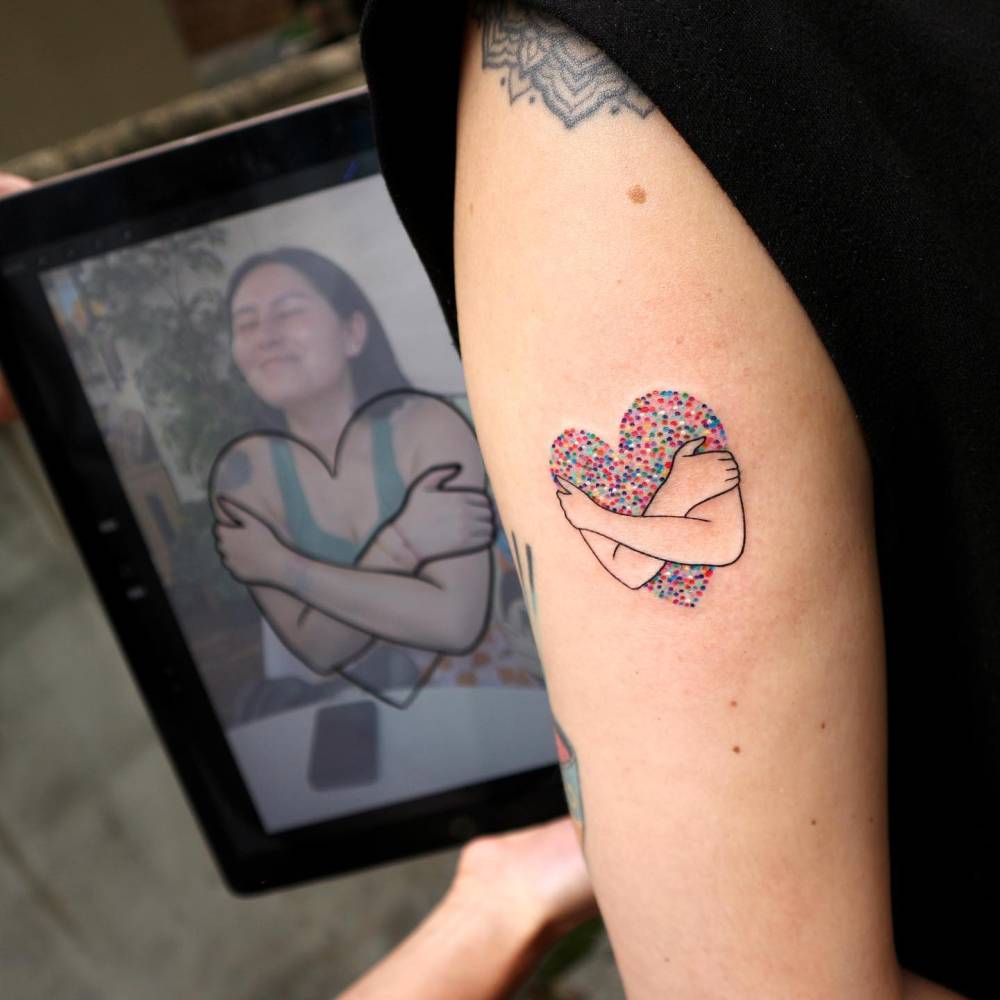 Self hug tattoo in illustrative style located on the upper arm.