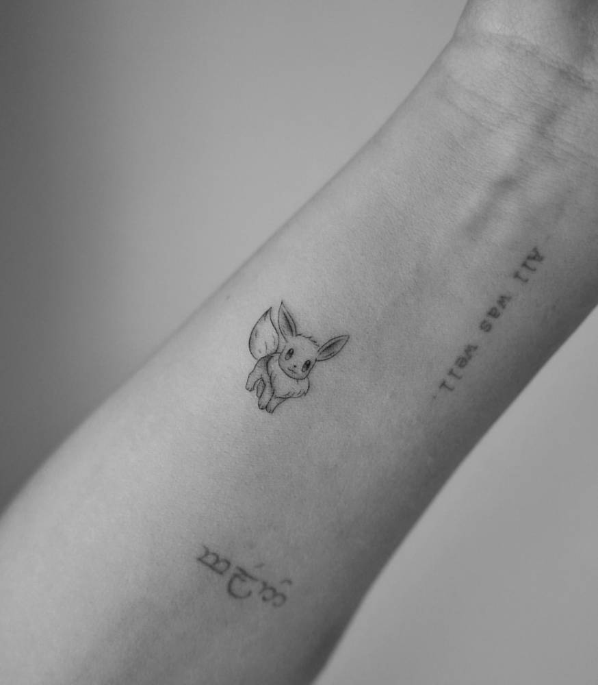 Tiny Eevee tattoo located on the wrist, cartoon style.