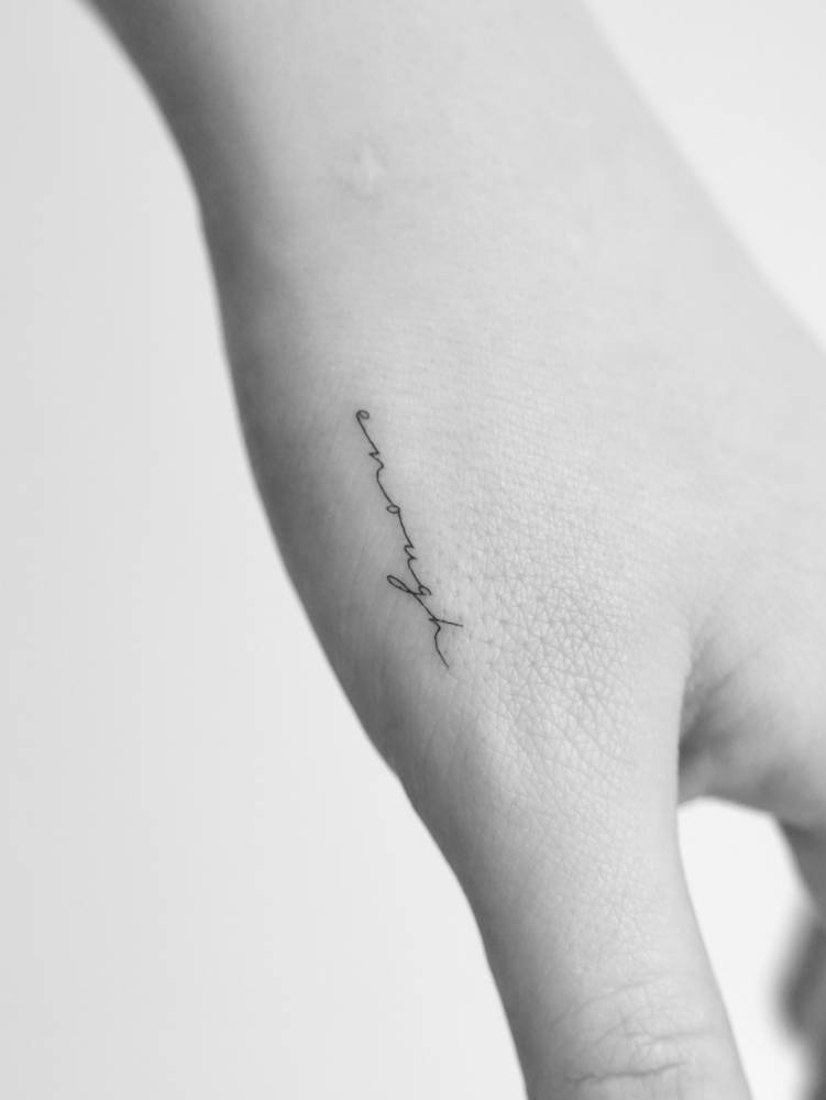 Handwritten font word "enough" tattooed on the hand.