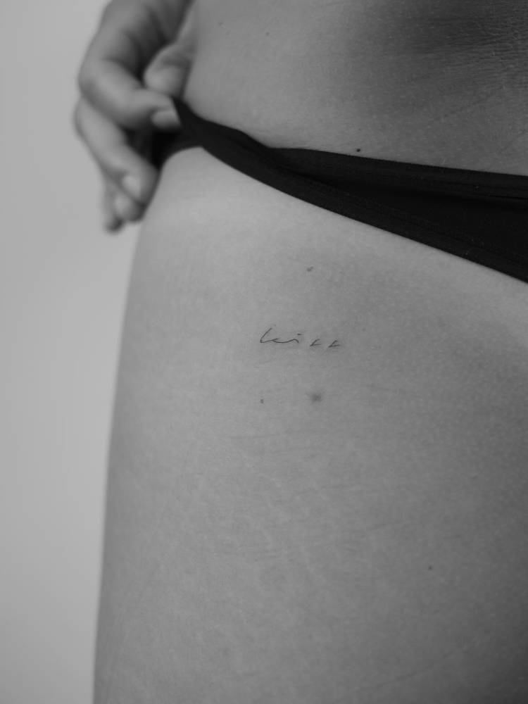 Handwritten font word "kiss" tattooed on the butt cheek.