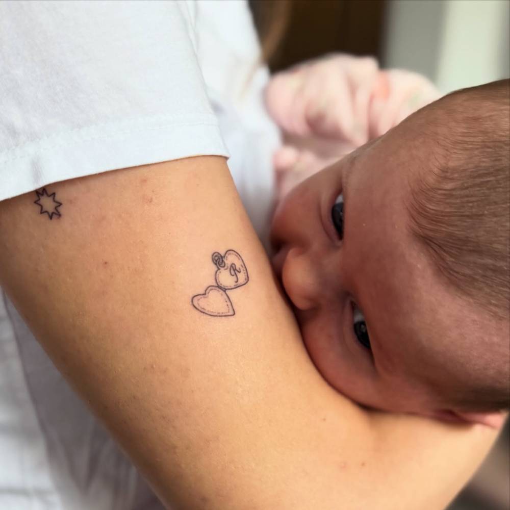 Hand poked heart pendant with the letter "R" tattoo located on the upper arm.