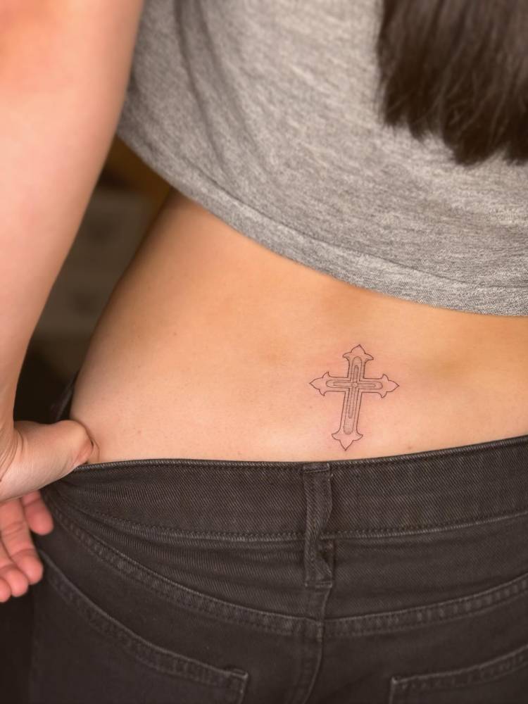 Cross tattoo in fine line style located on the lower back.