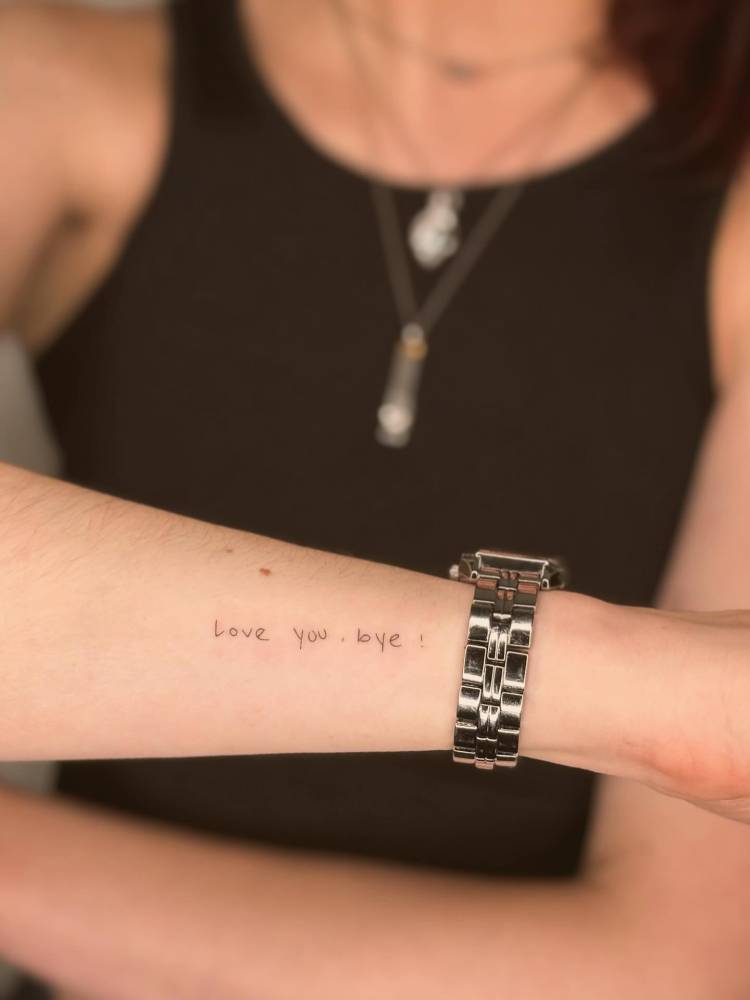 “Love you, bye” lettering tattoo in handwritten font located on the wrist.
