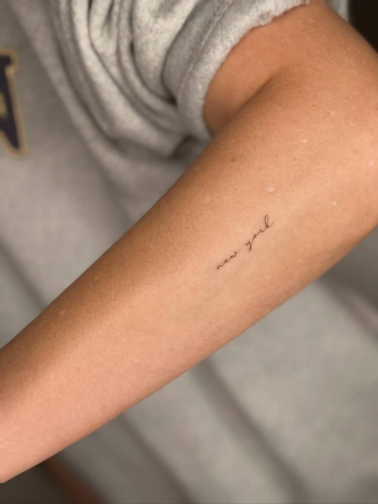 Handwritten font "New York" lettering tattoo done on the forearm.