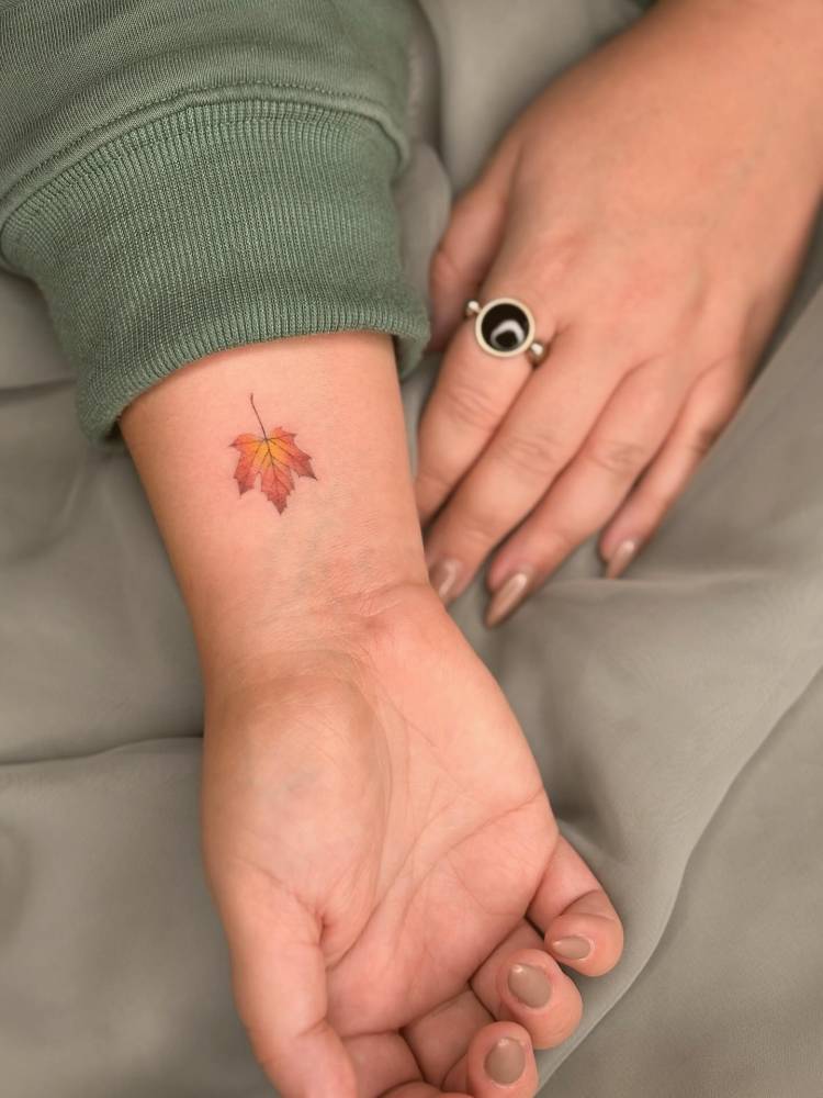 Watercolor style maple leaf tattoo located on the wrist.