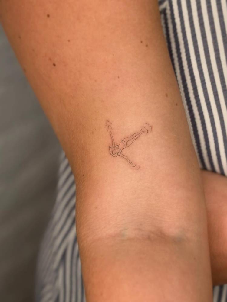 Little swimmer tattoo in fine line style located on the bicep.