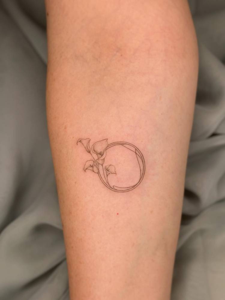 Calla lilies circle tattoo located on the inner forearm, done in fine line style.