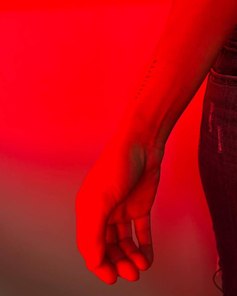 Word "listen" in handwritten font tattooed on the wrist.