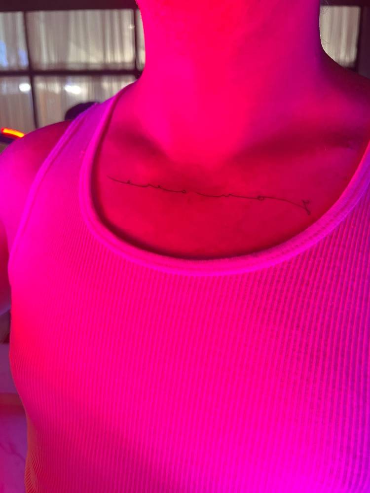 Mirror writing "you are" lettering tattoo located on the collarbone.