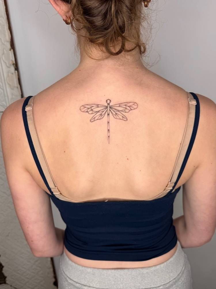 Illustrative style dragonfly tattoo placed on the upper back.