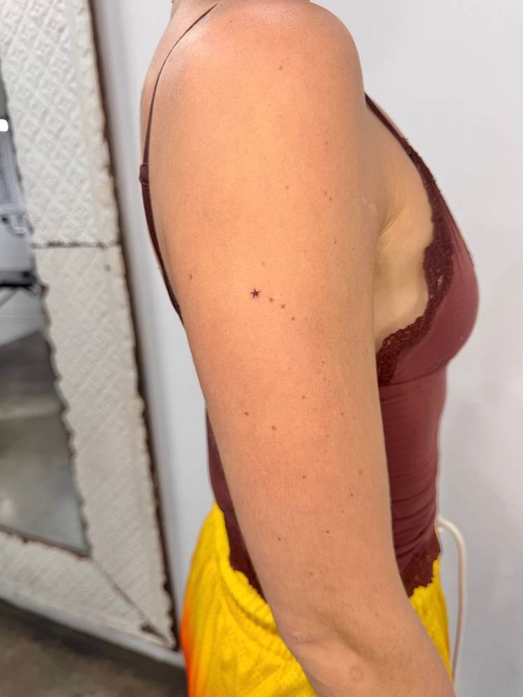Tiny minimalistic shooting star birthmark cover up tattoo located on the upper arm.